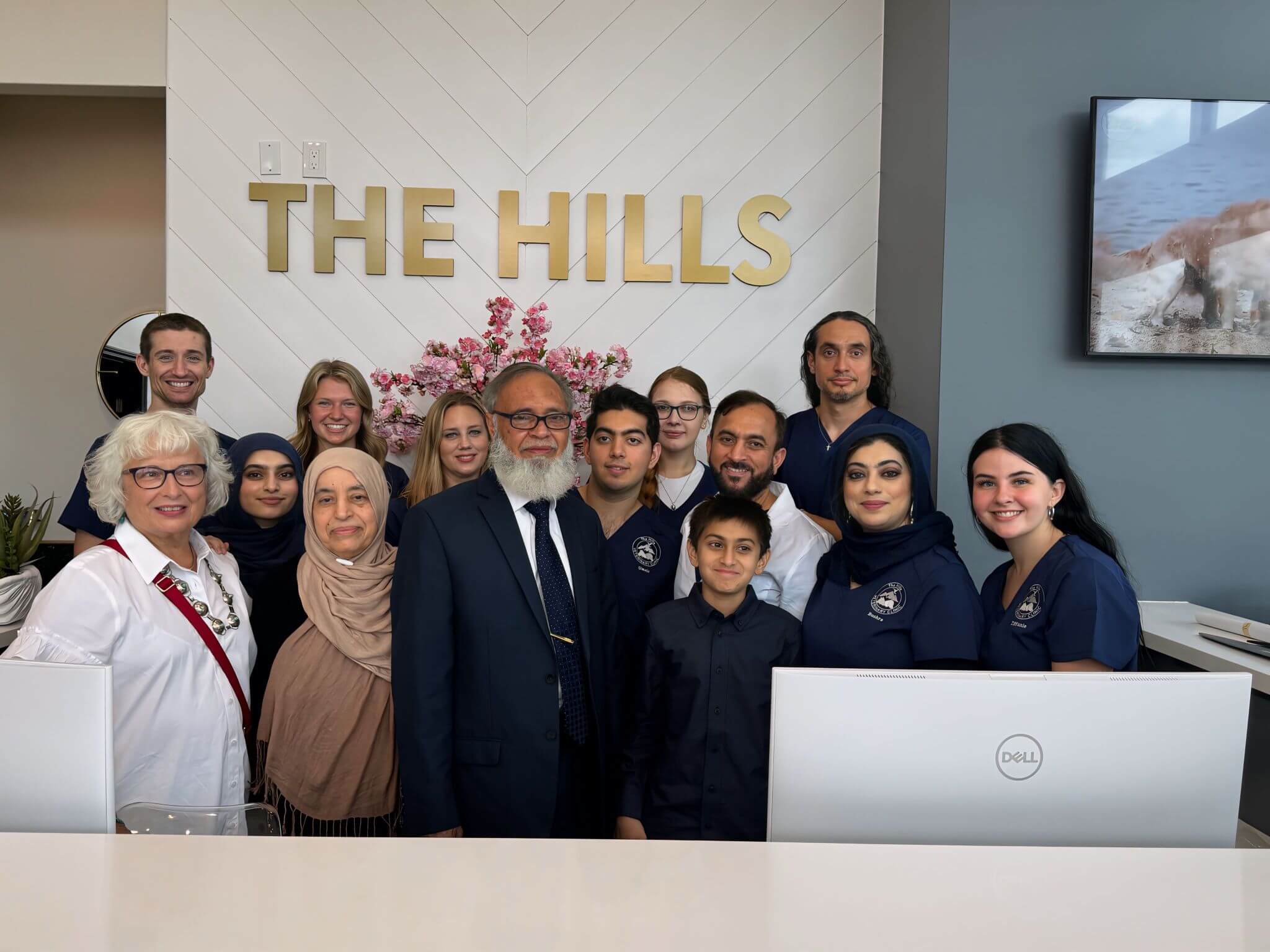 A group of people, some in uniform, pose together behind a front desk with "THE HILLS" sign on the wall.